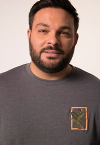 Šedé tričko s krátkým rukávem a kulatým výstřihem, s vyšitým designem rostliny v zelené a oranžové barvě na hrudi.