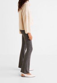 Beige knit sweater with a high collar and wide sleeves, paired with gray flared pants and white flat shoes. Textured fabric and relaxed fit.