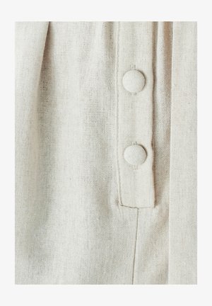 Tessuto beige chiaro con una trama texturizzata, caratterizzato da due bottoni rivestiti di tessuto sulla parte anteriore e un piccolo dettaglio di cucitura verticale.