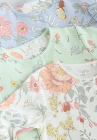Trois bodies pour bébés dans des couleurs pastel : bleu, vert et blanc. Motifs floraux, tissu en coton doux, boutons-pression et encolures rondes.