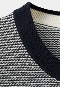 Tissu tricoté texturé noir et blanc avec un col côtes noir épais et une encolure intérieure blanche contrastante.