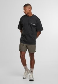 Černé př oversized tričko s potiskem loga, z párováno s olivovými šortkami. Na sobě béžové ponožky a stříbrné tenisky. Hladká textilie.