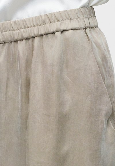 Μπεζ παντελόνι με ελαστική μέση, πλαϊνή ραφή και τσέπη, και ένα κατά το ήμισυ ορατό λευκό τοπ που είναι μισοφορεμένο μέσα.