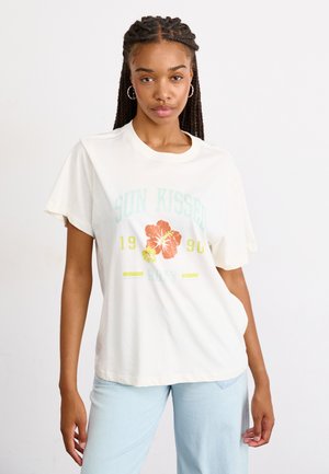 Kremasta pamučna majica s kratkim rukavima koja prikazuje šareni hibiskus s natpisom "SUN KISSED 1990 Roxy". Opušteni kroj, mekana tekstura.