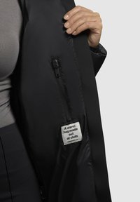 Sort dunjakke indeni, med en lynlås og et mærke, der siger "En varm omfavnelse lavet af stof." Glat, blank tekstur.