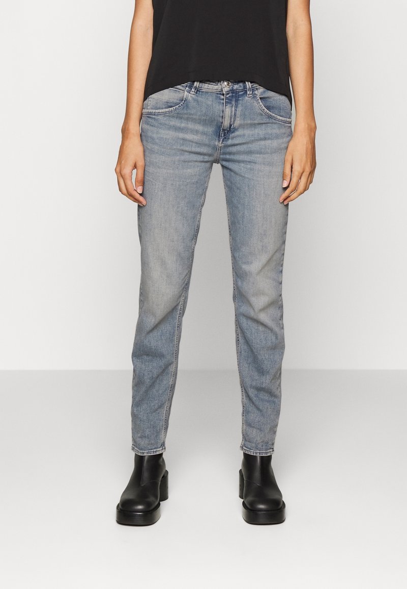 Jean en denim bleu clair à coupe ajustée, avec cinq poches, léger effet délavé et coupe droite, porté avec des bottines noires.