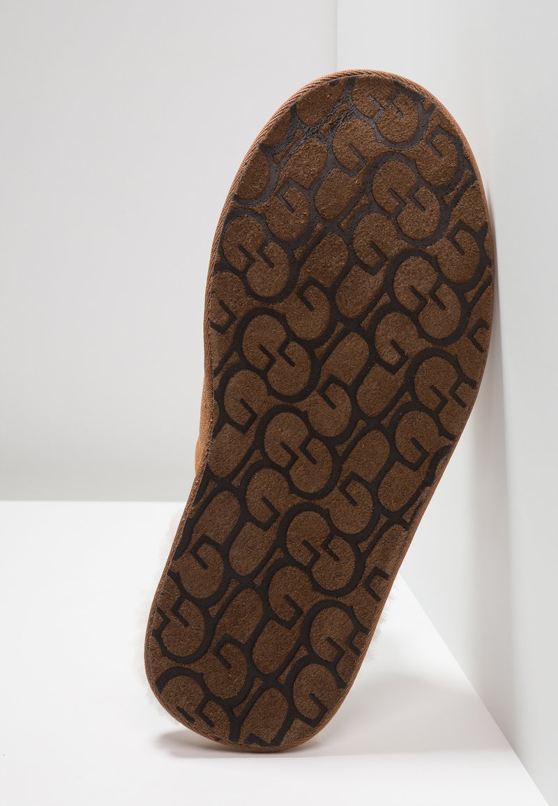 Brauner strukturierter Schuhsohle mit einem gemusterten schwarzen Logodesign. Abgerundete Form und samtartige Material, auf einem hellen Hintergrund platziert.