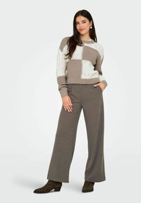 Maglione lavorato a maglia in crema e beige con motivi testurizzati, abbinato a pantaloni grigi a gamba larga. Modella che indossa stivali alla caviglia con tacco marroni.