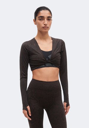 Kvinde iført sort cropped langærmet top med hul til tommelfingrene over en sort sports-bh og matchende højttaljede leggings med subtile mønstre.