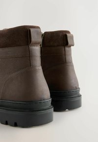 Braune Leder-Stiefeletten mit strukturierter Oberfläche, ausgestattet mit einem gepolsterten Kragen, einem Reißverschluss und einer schwarzen Gummisohle mit Profil.