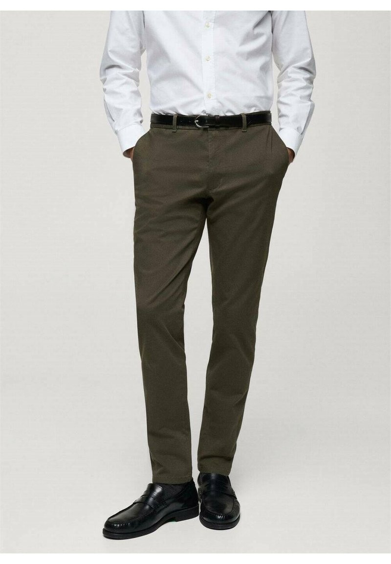 Pantalons habillés khaki avec une coupe ajustée, fabriqués dans un tissu lisse. Comprend des poches avant, une ceinture avec une boucle en métal argenté, associés à des chaussures noires.