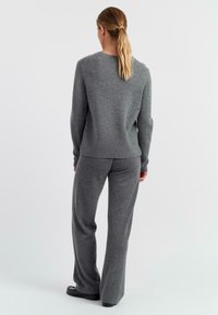 Grijze gebreide trui met een ronde halslijn, gecombineerd met ruime grijze broek. Beide items hebben een zachte textuur en een ontspannen pasvorm.