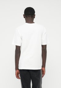 Baltas trumpomis rankovėmis medvilninis marškinėlis su apvalia apykakle ir tiesia apačia. Galia matomas minimalistinis dizainas be jokių grafinių elementų.