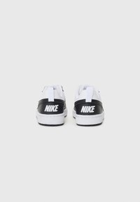 Sort-hvide Nike sneakers med overdel i læder, hvid sål og fremtrædende logo på bagsiden. Har et minimalistisk design.