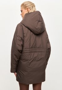 Bruine geïsoleerde parka jas met een capuchon, voorzien van een cinched taille en subtiele stikdetails, ontworpen voor warmte en comfort.