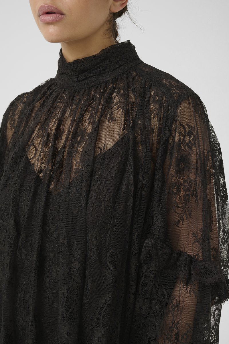 Black lace blouse featuring a high neckline, flowing silhouette, and ruffled accents on the sleeves. Intricate floral pattern throughout.