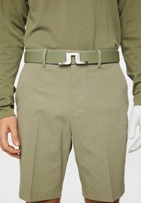 Oliivinvihreät shortsit, joissa on teksturoitu kangas ja tyylikäs metallinhohtoinen hopeinen vyönsolki, jossa on erottuva logomuotoilu.