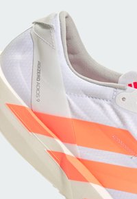 Λευκό αθλητικό παπούτσι με ροζ-πορτοκαλί αποχρώσεις, υφή στην επιφάνεια και μαξιλαρωμένο κολάρο. Διαθέτει εκτυπωμένο λογότυπο στο πλάι.