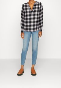 Blusa a maniche lunghe a scacchi bianco e nero con scollatura a V, abbinata a jeans skinny blu chiaro e scarpe slip-on color sabbia.