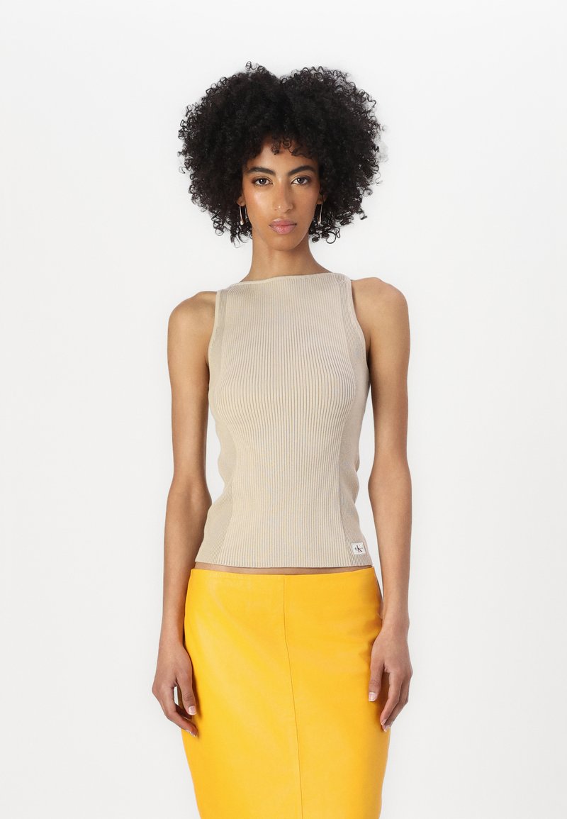 Beige ribadiga tank top, millel on ruudukujuline kaelus ja kitsad õlastrehvid, koos kollase nahkse seelikuga. Väike logo detail hemul.