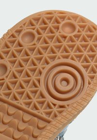 Semelle de chaussure en caoutchouc couleur beige clair, présentant un motif triangulaire et des éléments de design circulaires, avec une texture pour une meilleure traction et adhérence.