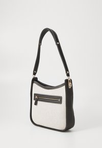 Sac à épaule noir et blanc avec un devant en tissu texturé, des accents noirs lisses, une poche zippée à l'avant et une sangle cousue.