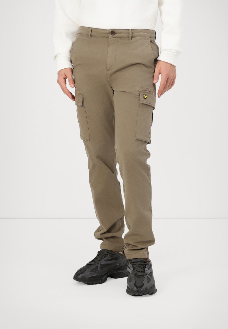 Cargo pants in olive green fabric feature two side pockets and a small logo patch. Paired with textured black sneakers.