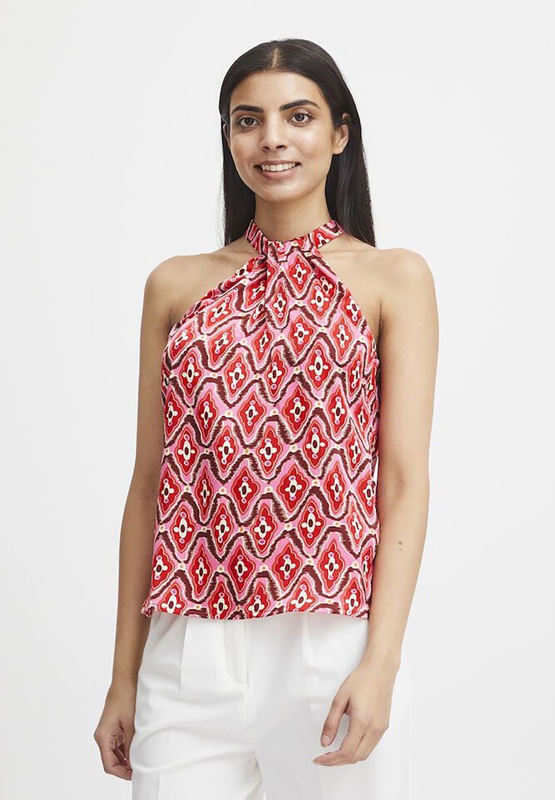 Top a halter rossa e rosa con motivo geometrico su un tessuto morbido, abbinato a pantaloni bianchi.