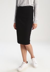 Černá tužková sukně vyrobená z texturované látky, s přiléhavým střihem a pasem. Spárováno s bílými teniskami pro ležérní vzhled.