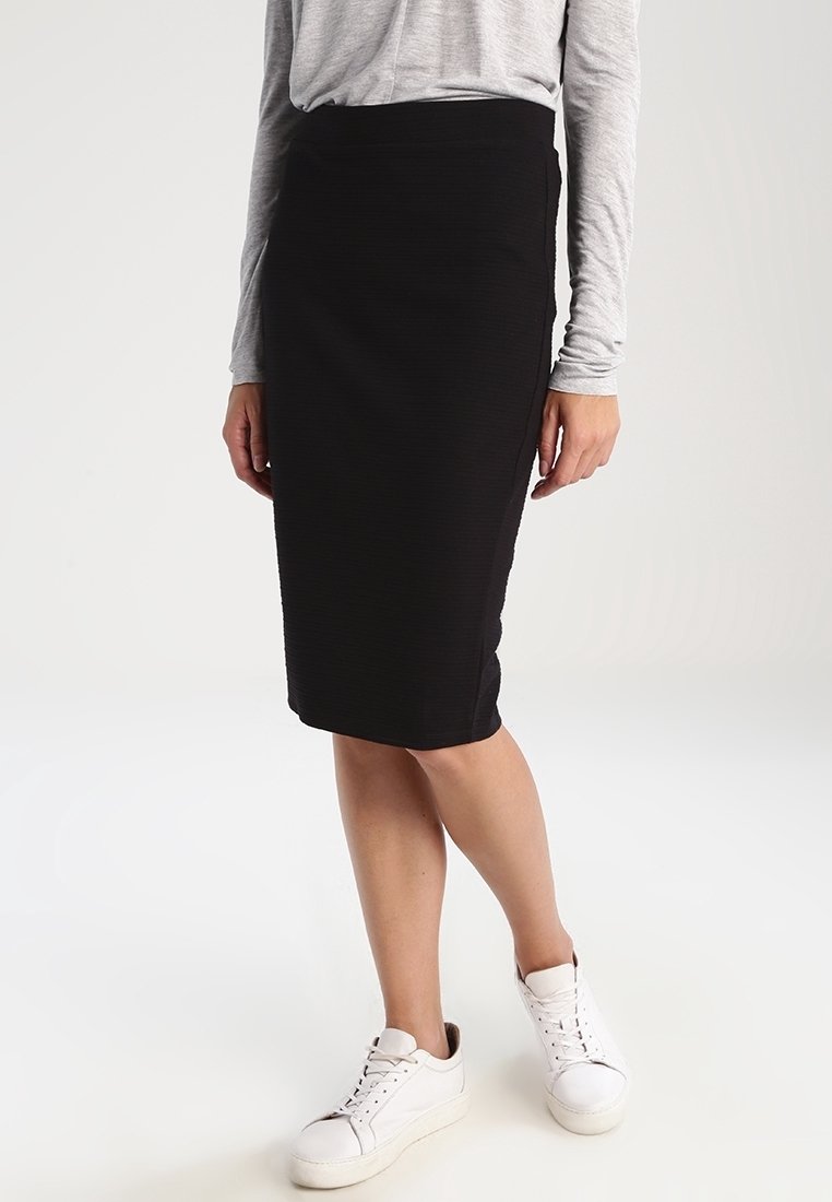 Černá tužková sukně vyrobená z texturované látky, s přiléhavým střihem a pasem. Spárováno s bílými teniskami pro ležérní vzhled.