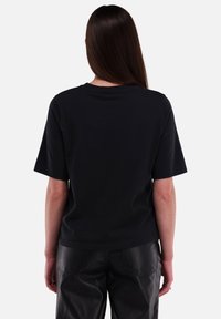 Zwarte t-shirt met korte mouwen van katoen, featuring een ronde hals, een gladde textuur en een relaxte pasvorm, getoond vanaf de achterkant met minimale details.