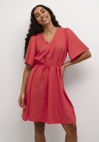 Robe corail mi-longue en tissu texturé, avec un décolleté en V, des manches courtes et une taille à nouer pour une silhouette ajustée.