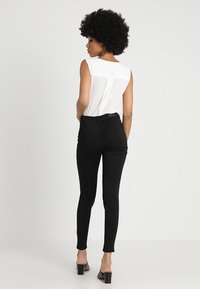 Jeans skinny noirs et un haut sans manches blanc, vus de l'arrière. Le haut a une texture subtile, les jeans ont une finition lisse et des poches arrière.