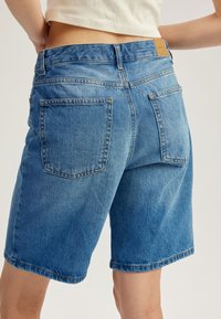 Pantalones cortos de mezclilla en azul claro, con un corte relajado, bolsillos traseros y un sutil detalle de costura en el dobladillo y la cinturilla.