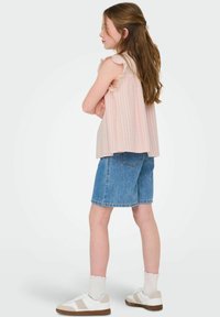 Ljusrosa randig topp med volangärmar, matchad med blå denimshorts. Vita sneakers med beige detaljer och ribbade vita strumpor.