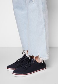 Námořnické plátěné tenisky s bílými gumovými podrážkami, červenobílými akcenty, šněrováním, kombinované s světle modrými potrhanými džínovými kalhotami.