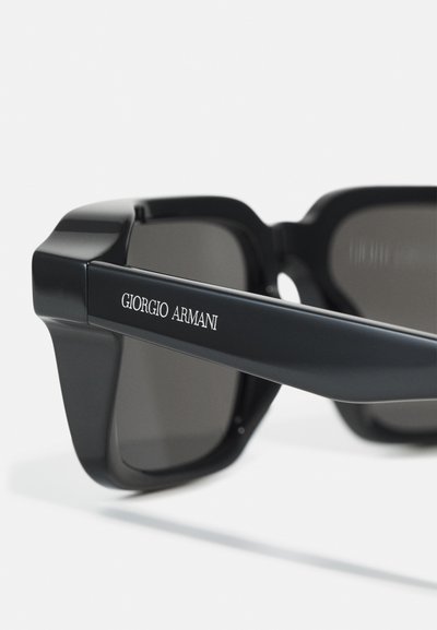 Mustad mustan ristkülikukujulised prillid tumedate läätsede ja kärme raamidisainiga, millel on tempel graveeritud "Giorgio Armani" logo. Sujuv tekstuur.