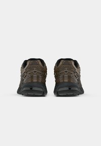 Brown athletic shoes featuring a textured upper, black accents, a cushioned sole, and a patterned design on the rear for improved traction.