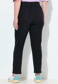 Vaqueros de mezclilla negros con una cintura alta, piernas ajustadas y dos bolsillos traseros. Combinados con zapatillas multicolores que tienen un acento turquesa.