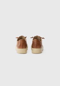 Chaussures en cuir marron avec une silhouette basse, un arrière arrondi, une semelle en caoutchouc beige et des accents de lacets décoratifs à l'arrière. Texture lisse.