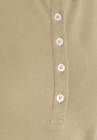 Gros plan sur un tissu beige texturé avec quatre boutons blancs alignés verticalement sur une patte, montrant les détails des coutures.