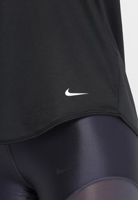 Camiseta deportiva negra de tela suave con dobladillo redondeado, con un logo blanco de Nike. Combinada con leggings morados brillantes.