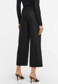 Zwarte wijde broek met een gladde textuur, elastische tailleband en enkel-lange snit, gecombineerd met zwarte open-teen hakken.