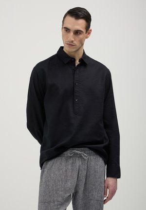 Camicia nera in lino a maniche lunghe con patta bottonata e colletto classico, abbinata a pantaloni grigi chiari a strisce con coulisse.