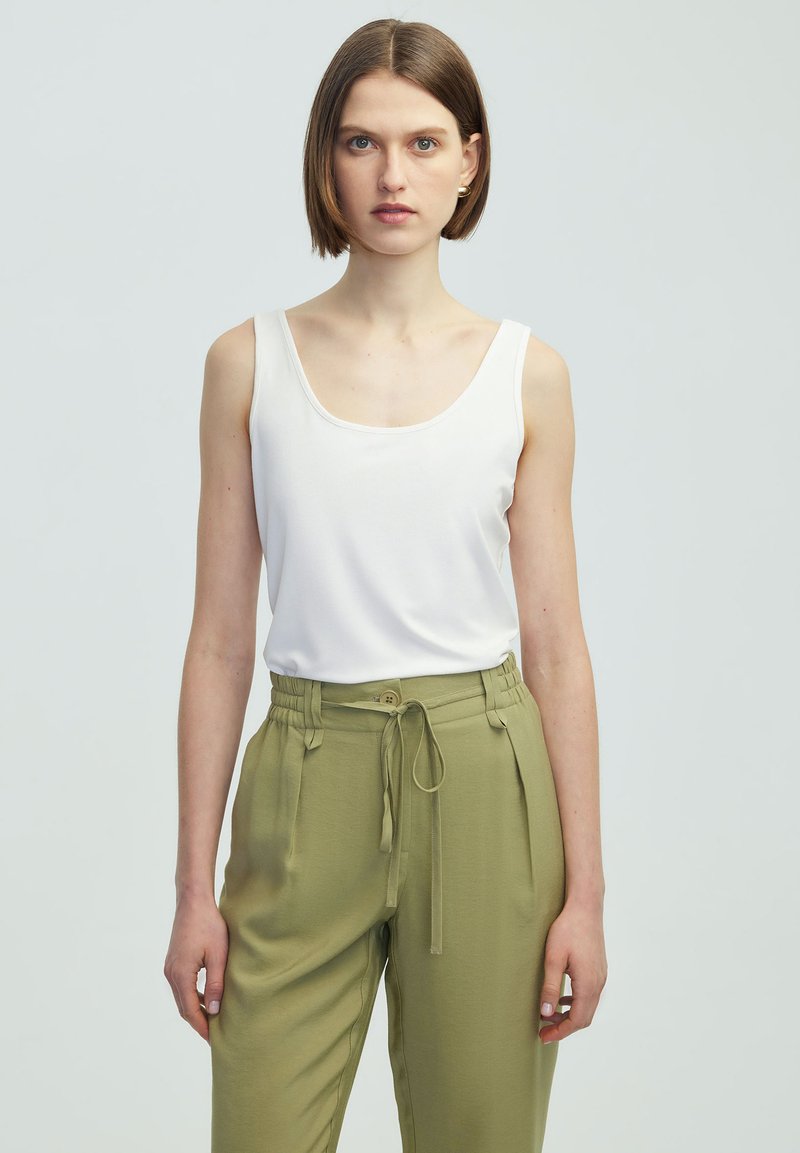 Top bianco senza maniche con scollatura a barchetta abbinato a pantaloni a vita alta verde oliva con coulisse e tasche laterali.