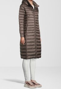 Ruskea puff takki hupulla, jossa on pystysuuntainen tikkikuosi. Yllä vaaleanväriset leggingit ja paksupohjaiset lenkkarit, joissa on sekoitus värejä.