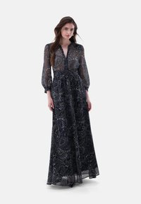 Abito lungo in tessuto trasparente di colore blu navy, con un motivo paisley, con bottoni sulla parte anteriore e maniche lunghe a palloncino. Design fluido con vita aderente.