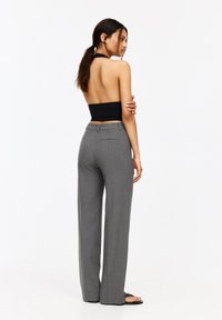 Pantalons gris sur mesure avec une coupe droite, confectionnés en tissu texturé, avec une poche arrière et une taille ajustée. Associés à un haut noir sans dos.