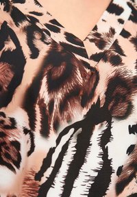 Topp med korte ermer har en V-hals, med et leopardmønster i nyanser av svart, brunt og krem. Stoffet virker glatt og lett.