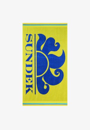 Asciugamano giallo brillante con grafica stilizzata di sole blu vivace e testo "SUNDEK" in verticale lungo il lato, caratterizzato da sottili strisce blu e verdi.